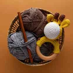 Handmade crochet materials and giraffe rattle arranged in a natural craft basket for Svamart